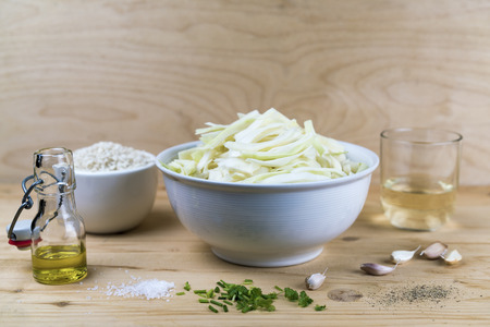 Bowl with sliced white cabbage, rice and glass and jar with oil, over wooden table background. Cooking conceptの写真素材