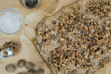 Homemade cake with roasted walnuts from above cropped shot of cake on baking paper with ingredients over wooden table surface backgroundの写真素材