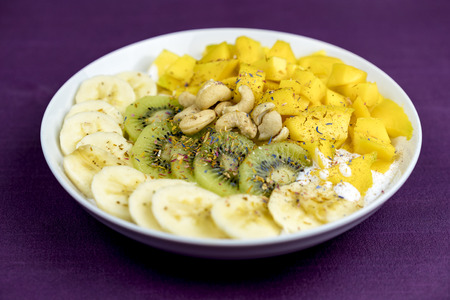 Plate of sliced fresh kiwi,mango, banana and cashew nuts arranged neatly on plate and seasoned with herbs and spice for a healthy dessert or snackの写真素材