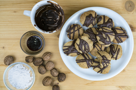 Tasty homemade walnut cookies displayed on a plate with an assortment of ingredients used in the baking of the recipe alongside, viewed from aboveの写真素材
