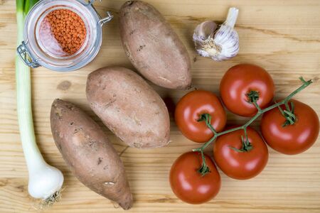 Fresh cooking ingredients for a homemade recipe with vine tomatoes, sweet potatoes, shallots, red lentils and garlic, overhead close up viewの写真素材