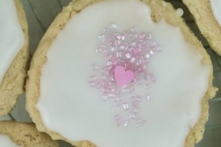 Close up overhead view of a delicious freshly baked homemade iced cookie with pink heart symbolising love and romanceの写真素材