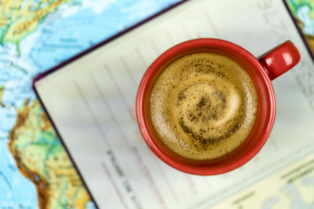 Freshly brewed cup of frothy espresso coffee and a passport on a map viewed from above in a concept of world travel and vacationsの写真素材