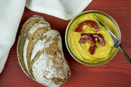 Rustic sliced rye bread and authentic homemade curry hummus with silver serving spoon garnished with beautiful red capsicum slicesの写真素材
