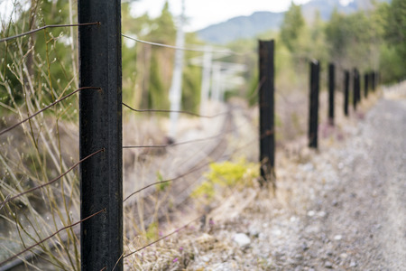 Rural fence dividing a country road from railway tracks with focus to the closest post and strands of wire over a blurred background in a receding perspectiveの写真素材