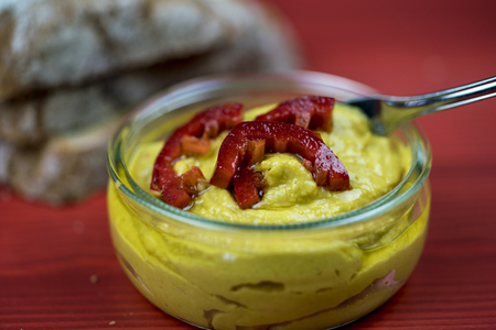 Selective focus close up view on spoon in curry hummus with hot red pepper slices over red surfaceの写真素材