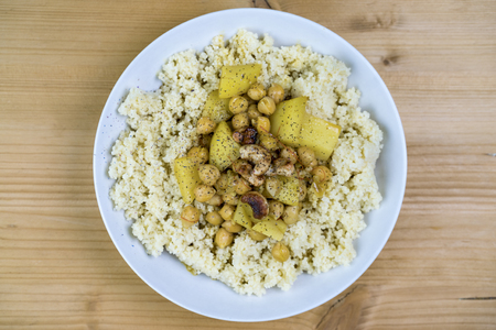 Plate filled with couscous, chickpeas and herbs over light brown wooden backgroundの写真素材