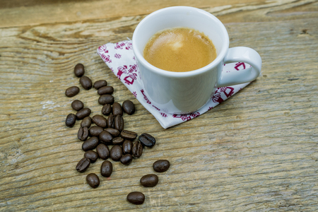 Coffee beans alongside a cup of milk coffee placed on a napkin on a cloth with copy spaceの写真素材