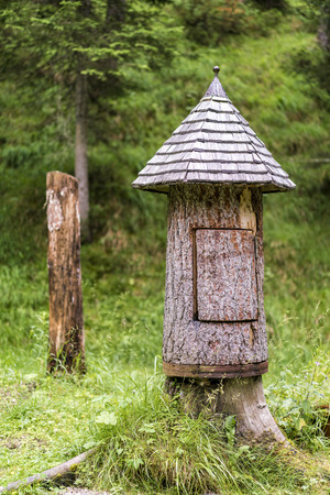 Rustic wooden tree hut in a forest formed from the trunk of a tree with a carved shingle roof standing in a green woodland gladeの写真素材
