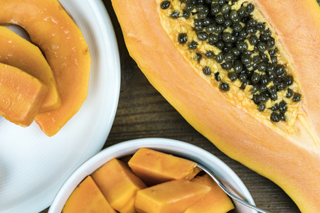 Close up view of papaya cut in half with black seeds next to small pieces in bowl against wooden backgroundの写真素材