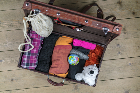 Open vintage suitcase of brown leather packed for the journey with rolled clothes, globe and polar bear toy as a mascot. Case is on the floor and viewed from aboveの写真素材
