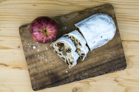 Sliced Christmas cake in white glaze with raisins, viewed in close-up from above on old wooden cutting board on the table with a whole apple . Copy spaceの写真素材