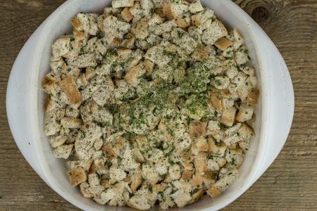 A close up, above view of a bowl of bread casserole seasoned with herbs on a timber table.の写真素材