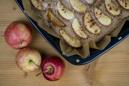 Cooked apple pie on paper in black baking tray with apples, viewed from above with unpainted wooden table surface in backgroundの写真素材