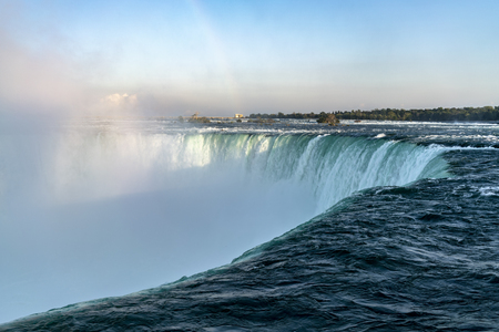 Close-up view of Niagara Falls, clouds of water mist and clear blue water, with green forest in backgroundの写真素材