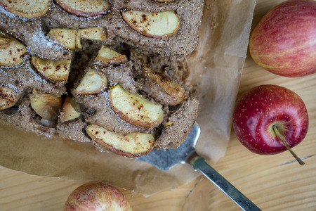 Taking the piece of apple pie with metal cake spatula. Fresh whole red apples also on the wooden table. Viewed in closeup from high angleの写真素材