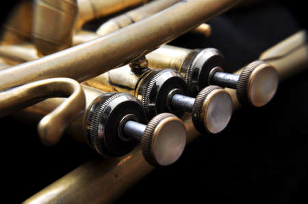 Close up of a valve section of an old professional trumpet with a black background behind.の写真素材