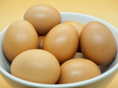 Side View Many Chicken Brown Eggs in the white bowl with orange background