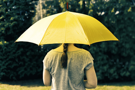 Young girl hiding under yellow umbrellaの写真素材