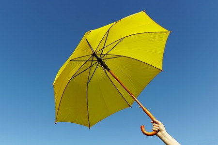 Yellow umbrella in the hand on the sky backgroundの写真素材