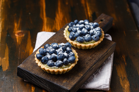 Two tartlets with lemon custard and blueberries on the wooden surfaceの写真素材