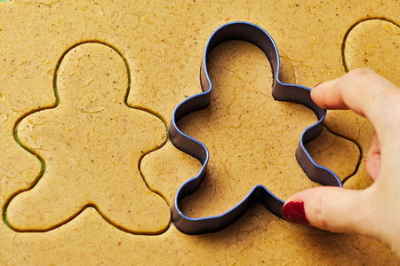 Female hand making christmas gingerbread men cookies with metal cutterの写真素材