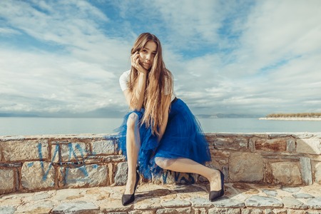 Pretty young girl in blue pettiskirt  seating on stonesの写真素材