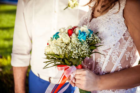 Beautiful wedding bouquet with red, blue and white roses in hands of the brideの写真素材