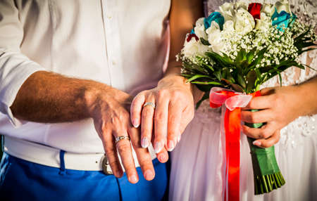 groom and bride hands with wedding rings and flowers