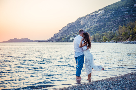back view of happy young couple in white on the beachの写真素材