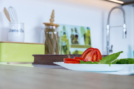 Tomato with salad in the white plate on the kitchen tableの写真素材