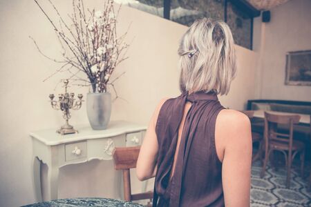Toned picture of back view of beautiful blonde lady sitting in cafe or restaurantの写真素材