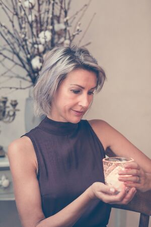 Toned picture of beautiful blonde lady sitting in cafe or restaurant holding candleの写真素材