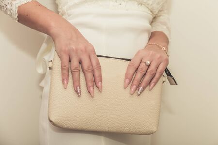 The bride in a wedding dress holds in hand a white bag. Beautiful manicure. Wedding day. Wedding rings.の写真素材