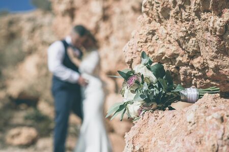 wedding bouquet of green and white flowers on the stone with bride and groom in backgroundの写真素材