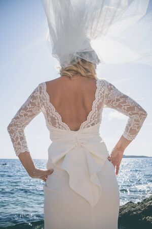 Beautiful bride in luxury wedding dress at the sea side. Wedding by the sea. Bride walking around the sea near the place of the wedding ceremony. Back viewの写真素材