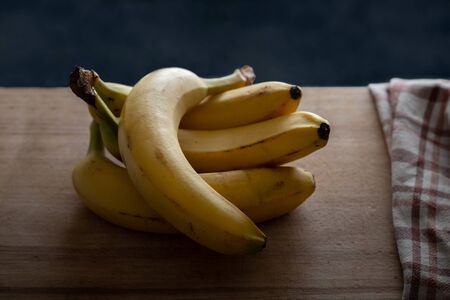 several fresh bananas lauing on wooden cutting boardの写真素材