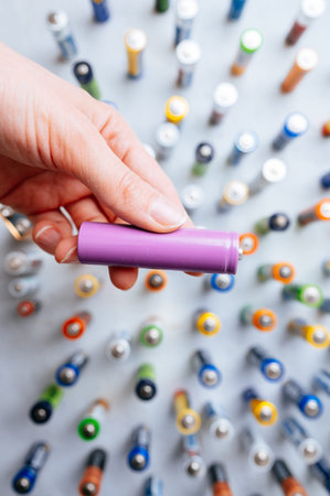 Closeup Of Hand Holding Purple Battery With Technician Assessing Batteries In Background