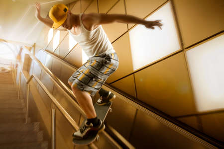 young skateboarder with basecap and shorts sliding down stairs in front of yellow background and...