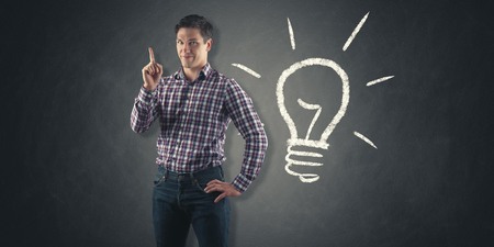 young man in front of chalkboard with light bulb drawn on it has an ideaの写真素材