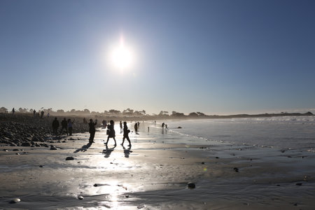 People walking on the beach at low tide with sun in the background