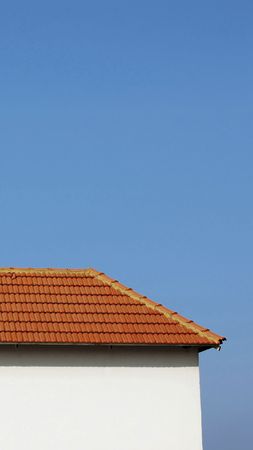 The half part of a tiled rooftop and white side of a house against a blue sky.
