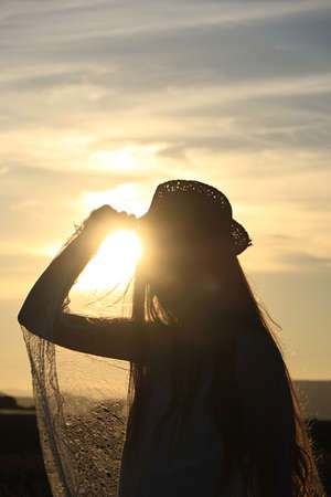 A girl's silhouette against the sun with flying golden hair, she's wearing a hat.の写真素材