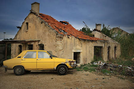 A yellow old car parked in front of a crumbling abandoned house.の写真素材