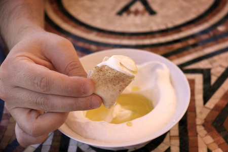A man dipping a pita bread slice in labneh and offering it.の写真素材