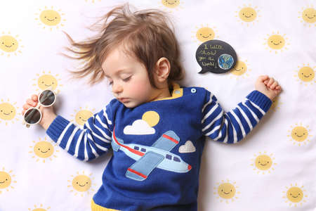 A sleeping baby wearing an airplane shirt and holding sunglasses dreamining of traveling, with a...