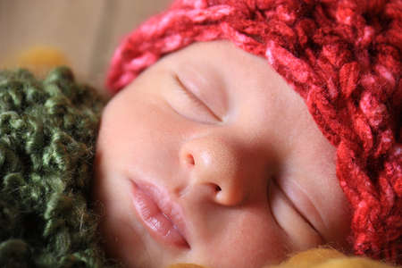 A sleeping newborn wearing a fluffy red hat and covered in a solft wool blanket.