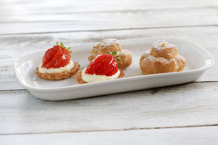 A plate of strawberry tarts and cream puffs pasteries.