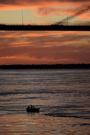 men at a distance on lonely boat under bridge Manuel Belgrano on Parana river, Corrientes, Argentinaの写真素材