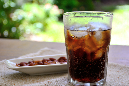 fresh cola in a glass with a snak of peanuts on a wood tableの写真素材